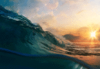 Sunset over the ocean with a rising wave in the foreground, highlighting warming seas amid global climate change concerns.