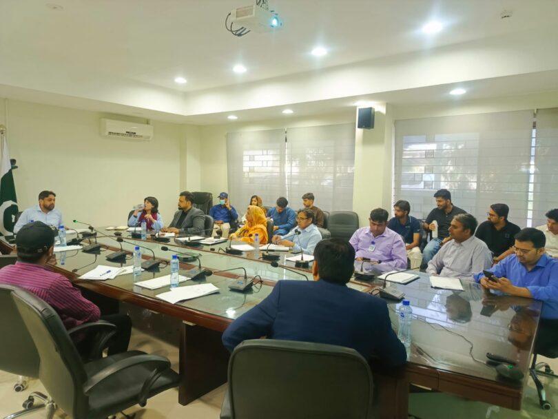 کانفرنس روم میں ایک رسمی اجلاس کا منظر، جہاں شرکاء ایک بڑی میز کے گرد بیٹھے ہوئے ہیں۔ میز پر مائیکروفون، دستاویزات اور پانی کی بوتلیں موجود ہیں جبکہ شرکاء توانائی تحفظ اور صنعتی ترقی سے متعلق گفتگو اور مباحثے میں مصروف ہیں۔